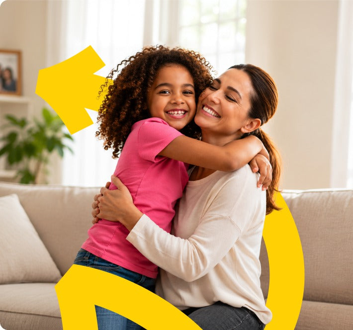 A mother and daughter hugging on a sofa at home.
